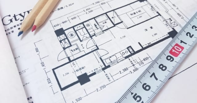 住宅の間取り図の上に赤青の色鉛筆とメジャーが置かれている