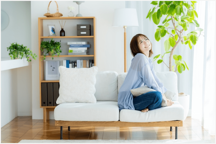 明るいリビングで白いソファに座り、リラックスした笑顔を見せる女性